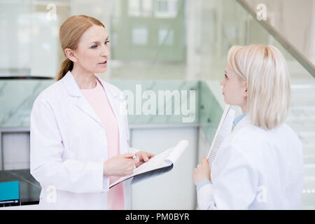 Zwei junge Ärzte in whitecoats diskutieren arbeiten Momente und Papiere im Krankenhaus Stockfoto