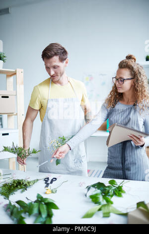 Junge Frau in Schürze zeigen im Bracken verlässt, während IT-Angebot für florale Komposition Stockfoto