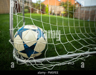 Ein Fußball ist eingebettet in die Rückseite des Netzes in einem Garten auf der Rückseite Stockfoto