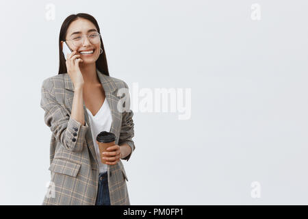 Im Gespräch beiläufig mit Freund während der Mittagspause. Gerne gut aussehende stilvolle Frau in Gläsern und Jacke, Tasse Kaffee und Smartphone, lustige Gespräche, erfreuen sich großer Tag Stockfoto