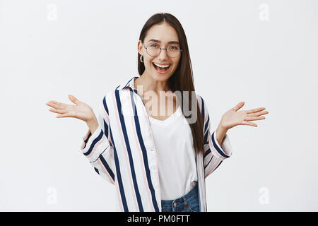 Wer sich interessiert, lass uns Spaß haben. Portrait von amüsiert gut aussehende sorglos Studentin im stilvollen gestreiftes Hemd und Brille, Palmen beiseite Verbreitung während breit grinsend, führenden sozialen Lebensstil Stockfoto