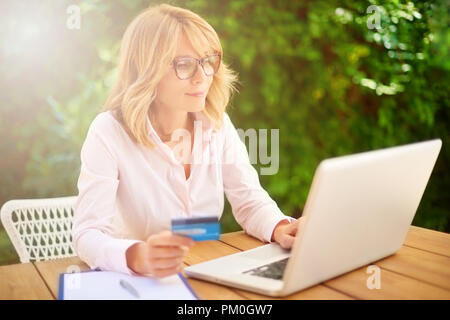 Hohe Aufnahme von attraktiven Frau mittleren Alters mit Laptop und Kreditkarte beim e-Banking von zu Hause aus. Stockfoto