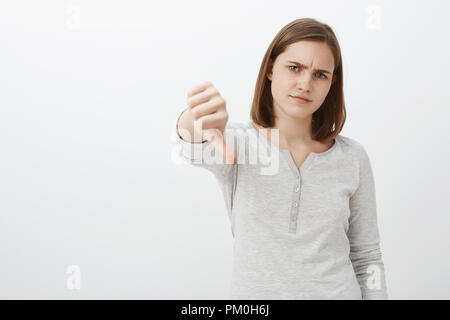 Langweilig und unscheinbar Geschichte. Portrait von unbeeindruckt Missfallen pingelig Mädchen mit kurzen braunen Haare stirnrunzelnd schürzte die Lippen aus Abneigung, Daumen nach unten zum Ausdruck Abneigung und Antipathie Stockfoto