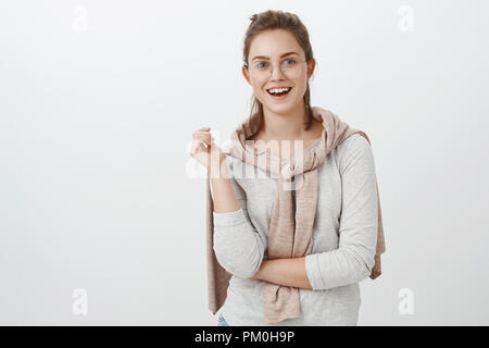 Taille-up Shot der geselligen gut amüsiert suchen europäische Frau mit gekämmte Haare in Gläsern und Pullover über Hals Gestik beim Reden gebunden und lächelte breit Gefühl interessiert im Gespräch Stockfoto