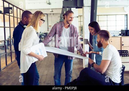 Als Team arbeiten. Volle Länge des jungen modernen Menschen in Smart Casual Wear planning Business Strategie, während junge Frau zeigt auf großem Papier im Büro Flur. Stockfoto