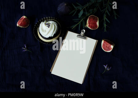 Dunkle essen immer noch Leben. Lila Feigen auf Leinen Tischdecke Reif. Grußkarte mockup in binder Clip. Vintage moody Komposition mit Obst, Kuchen, Eukalyptus, Zweige und Blüten. Flach, Ansicht von oben. Stockfoto