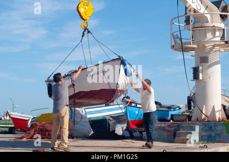 Männer heben Fischerboot in Wasser mit Bootskran setzen Stockfoto