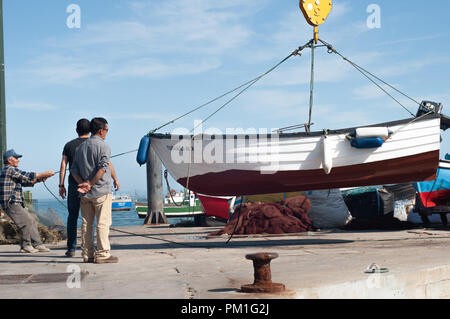 Männer heben Fischerboot in Wasser mit Bootskran setzen Stockfoto