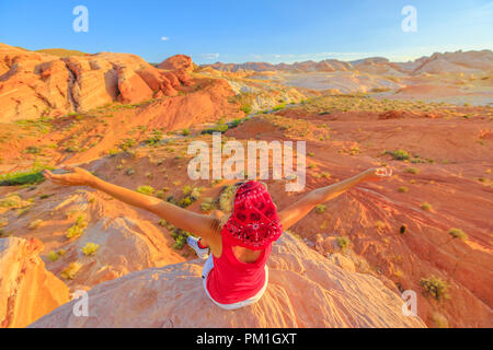 Freiheit wandern Frau in der Valley of Fire State Park auf Fire Wave bei Sonnenuntergang. Happy Wanderer mit Panoramablick auf Bänder des roten Felsens schnitt durch die Wüstenlandschaft. Nevada, United States. Stockfoto