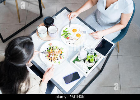 Hohen winkel Porträt von zwei jungen Frauen genießen das Frühstück im Cafe, auf schönen Gerichte auf den Tisch konzentrieren Stockfoto