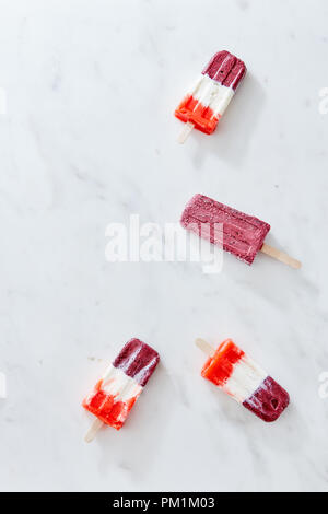 Ein Satz von vier mehrfarbige Obst Eis auf einem Stick in Form einer Ecke Frame auf grauem Marmor Hintergrund mit einer Kopie Raum vorgestellt. Flach Stockfoto