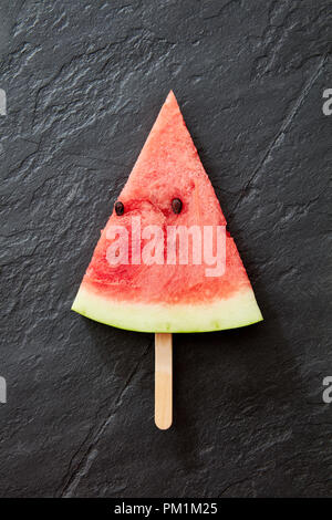 Eine Komposition von süßen Stück Wassermelone auf einem schwarzen konkreten Hintergrund. Ein Stück Wassermelone in Form eines Eis lolly eine Kopie. Gesunder Nachtisch. Flach Stockfoto
