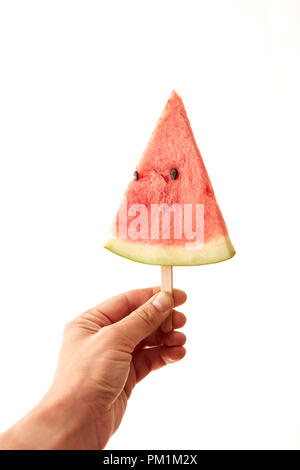 Eine dreieckige Scheibe einer Wassermelone auf einem Stock eine männliche Hand auf einen weißen Hintergrund mit Kopie Raum zu halten. Konzeption von Berry ice cream Stockfoto