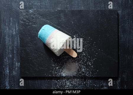 Bunte Eis auf einem Stick mit Kokosnuss crumb auf schwarzem Schiefer auf einem dunklen konkreten Hintergrund mit Kopie Raum dargestellt. Flach Stockfoto