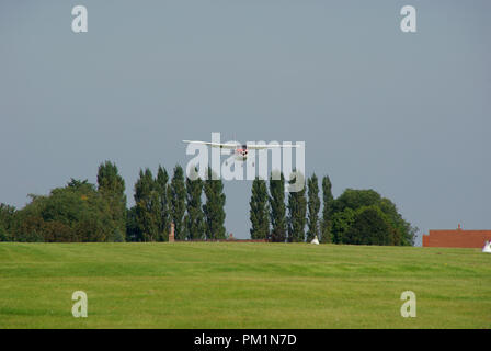 Eine Cessna Lichtebene kommen in eine Landschaft Gras Flugplatz mit einer Reihe von hohen Bäumen in der Nähe der Ansatz Land, mit Häuser in der Nähe. Elmsett Stockfoto