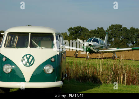 Die farbigen VW Camper van und Piper Cherokee Pfeil Light Aircraft Flugzeug auf einem kleinen Feld Gras Flugplatz. Klassische zeitlose Zeitraum Landschaft Stockfoto