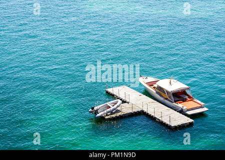 Ein Luxus Speedboot günstig zu einem isolierten, T-Form, Holz- Dock im grünen Wasser mit einem Beiboot auf dem Dock. Stockfoto