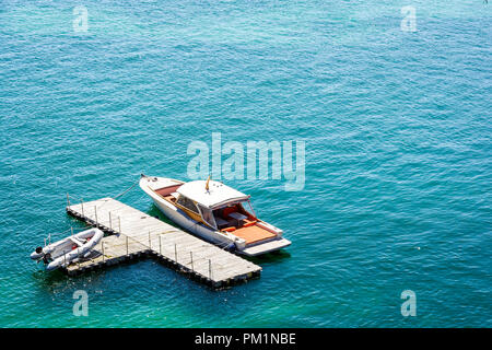 Ein Luxus Speedboot günstig zu einem isolierten, T-Form, Holz- Dock im grünen Wasser mit einem Beiboot auf dem Dock. Stockfoto