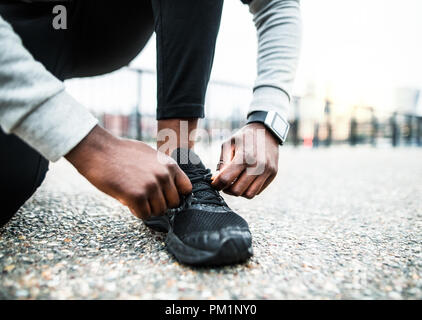 Eine Nahaufnahme eines jungen sportlichen schwarzer Mann runner Schnürsenkel binden außerhalb in einer Stadt. Stockfoto