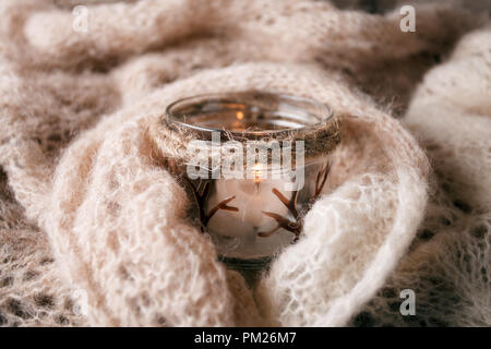 Kerzenlicht weißen Strickpullover auf der Plank Holz Tisch am Fenster. Gemütliche Winter Herbst Abend. Natürliches Licht Authentische ruhige Atmosphäre. Kinfolk Hygge Stockfoto