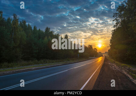 Asphalt im hellen Strahlen der aufgehenden Sonne mit einem schönen bewölkten Himmel. Stockfoto