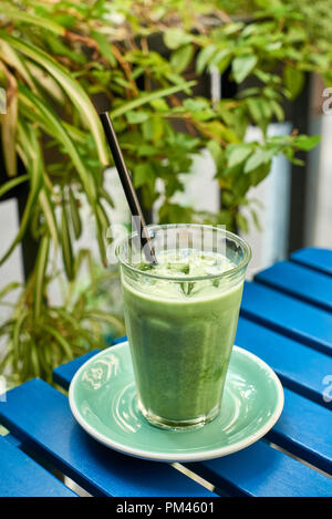 Iced Matcha Latte in Glas mit Strohhalm auf dem blauen Hintergrund (Holz- Tabelle) Stockfoto