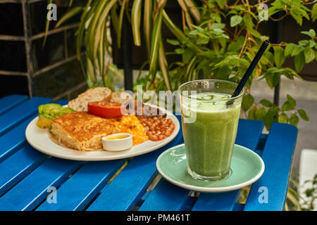 Englisch vegetarisches Frühstück mit Bohnen, Avocado, Tomate, Pilz und iced Matcha Latte in Glas Stockfoto