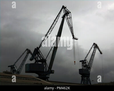 Ein paar riesige heben, Industriekrane, sitzen vor einem dunklen Himmel silhouetted, wie die riesigen Vögel, am Kai in Port Glasgow auf den Firth of Clyde in Schottland. Stockfoto