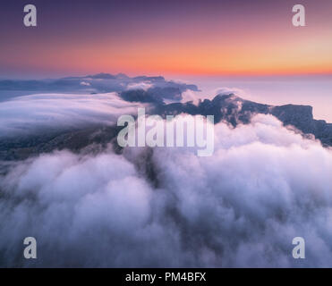 Luftaufnahme von niedrigen Wolken, Berge, Meer und bunten Himmel bei Sonnenuntergang. Über den Wolken in der Abenddämmerung. Seashore in Spanien. Ansicht von oben von drohne. Erstaunlich Landsc Stockfoto