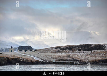 Niedrige Wolken teilweise verdecken die schneebedeckten Berge hinter Videy Insel in der Nähe von Reykjavik, Island Stockfoto