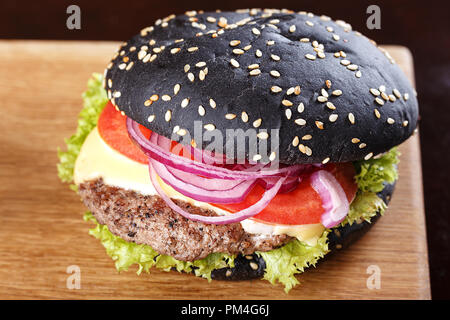 Schwarz Burger auf dem Brett mit Bratkartoffeln, Schnitzel, Gemüse und Käse; auf einem Holzbrett Stockfoto