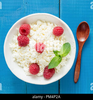 Quark, Landwirte, Käse, Ricotta oder Tvorog in Schale mit frischen Himbeeren auf Blau Holz- Hintergrund. Gesunder Lebensstil, Diäten, Fitness Concept Stockfoto