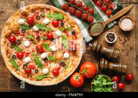 Leckere italienische Pizza mit Tomaten Mozzarella Rucola auf Holz- Hintergrund. Tabelle Ansicht von Oben Stockfoto