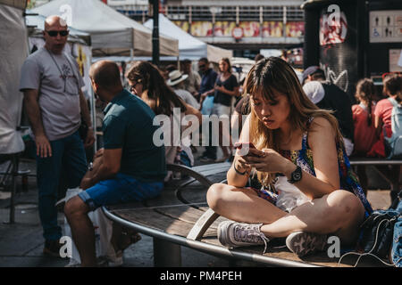 London, Großbritannien - 21. Juli 208: junge Frau allein auf einer Bank sitzen in Portobello Road Market, mit Ihrem Mobiltelefon. Portobello Road Market ist einer der Th Stockfoto
