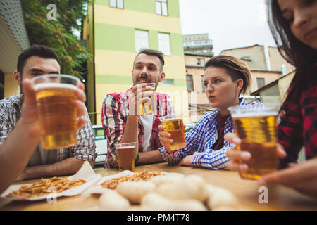 Die Gruppe der Freunde genießen und trinken Bier an der Bar im Freien oder im Pub. Gekocht serviert mit Weißwurst, Bier und Brezeln. Perfekt für Oktoberfest. Natürliche Holz- Hintergrund. Vorderansicht mit weiblichen und männlichen Händen Stockfoto