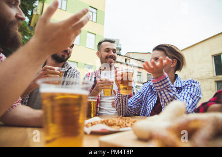 Die Gruppe der Freunde genießen und trinken Bier an der Bar im Freien oder im Pub. Gekocht serviert mit Weißwurst, Bier und Brezeln. Perfekt für Oktoberfest. Natürliche Holz- Hintergrund. Vorderansicht mit weiblichen und männlichen Händen Stockfoto