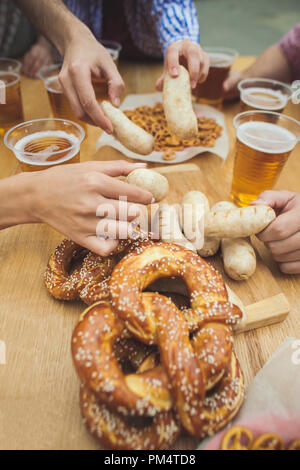 Gekocht serviert mit Weißwurst, Bier und Brezeln. Perfekt für Oktoberfest. Natürliche Holz- Hintergrund. Vorderansicht mit weiblichen und männlichen Händen Stockfoto