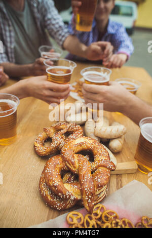 Gekocht serviert mit Weißwurst, Bier und Brezeln. Perfekt für Oktoberfest. Natürliche Holz- Hintergrund. Vorderansicht mit weiblichen und männlichen Händen Stockfoto