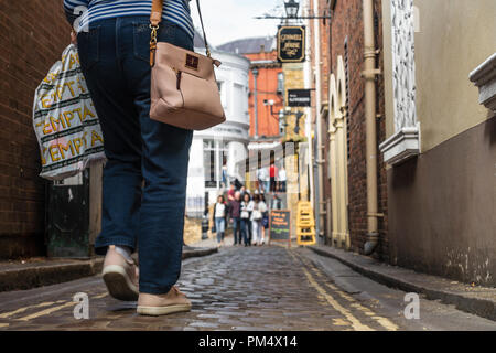 Niedrigen Winkel, Boden aus Sicht eines weiblichen Shopper mit Tragetasche und Handtasche hinunter eine schmale Straße in Windsor, UK. Stockfoto