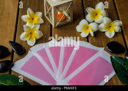 Rosa kalten waz Streifen auf Holz- Oberfläche mit plumeria Blumen, schwarze runde Steine und orange Kerze Stockfoto