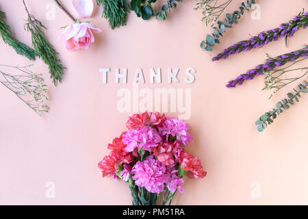 Dank Holz- wort mit frischen Blumen Nelken auf weiche Creme rosa Hintergrund Stockfoto