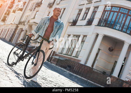 Zeitvertreib. Junge Mann zu Fuß auf der Straße mit dem Fahrrad zur Seite schauen, Lächeln, Freude Stockfoto