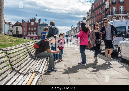 Ein Mann sitzt auf einer Bank ausserhalb Schloss Windsor auf Thames Street in Windsor als Touristen vorbei. Stockfoto