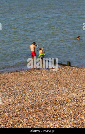 Eine Falther und Sohn Fisch für Krebse am Strand von Herne Bay, eine Frau in der Nähe schwimmt, Kent, Großbritannien Stockfoto