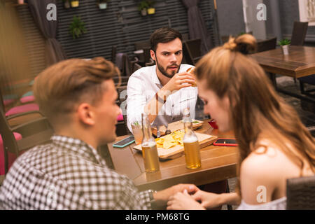 Junge Mann in seltsames Gefühl, während seine Freunde sehen Flirten Stockfoto