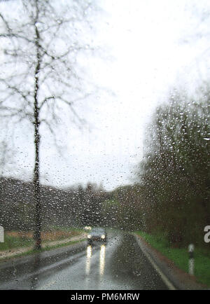 Ein Auto mit Scheinwerfern gesehen durch ein Regentropfen - überdachte Windschutzscheibe. Stockfoto