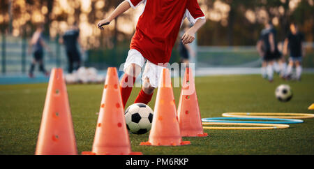 Fußball-Bohrer: Der Slalom Bohren. Jugend-fußball-Übungen. Jungen Fußball-Training der Tonhöhe. Fußball slalom Konus bohren. Jungen in roten Jersey Stockfoto