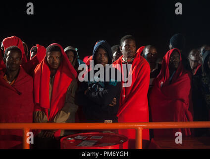 Migranten mit roten Decken, die aus einem beiboot im Mittelmeer gerettet wurden, gesehen werden, die in ein Rettungsboot nach ihrer Ankunft am Hafen von Malaga in einer regnerischen Nacht aussteigen. Mitglieder der Spanischen Sicherheit auf See gerettet Insgesamt 161 Migranten an Bord verschiedenen Jollen vom Mittelmeer und brachte sie nach Malaga Hafen, wo sie durch das Spanische Rote Kreuz unterstützt wurden. Stockfoto