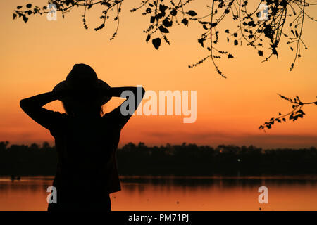 Silhouette einer jungen Frau entspannende gegen schönen leuchtenden Farben sonnenuntergang himmel von der Waterfront Stockfoto