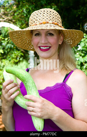 Frau in ihrem Garten arbeiten tragen, Sonnenhut und Holding Squash oder Blumen. Grüne Blumen und Pflanzen. Stockfoto